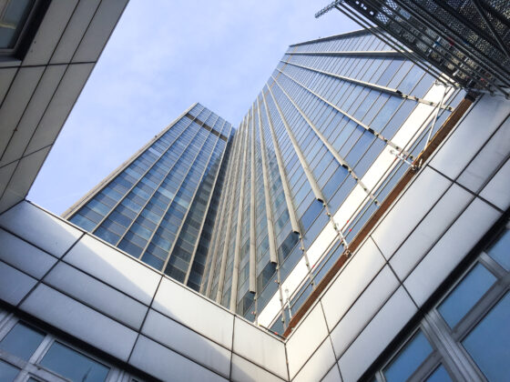 Blick nach oben auf moderne Wolkenkratzer mit Glasfassade und klar blauem Himmel.