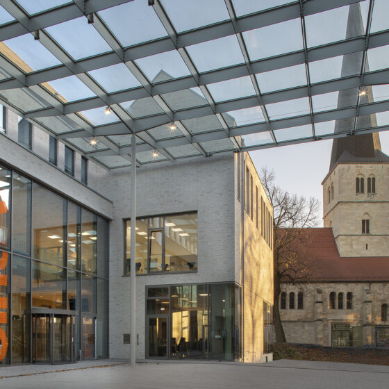 Moderne Architektur mit Glasdach und historischem Kirchturm im Hintergrund.