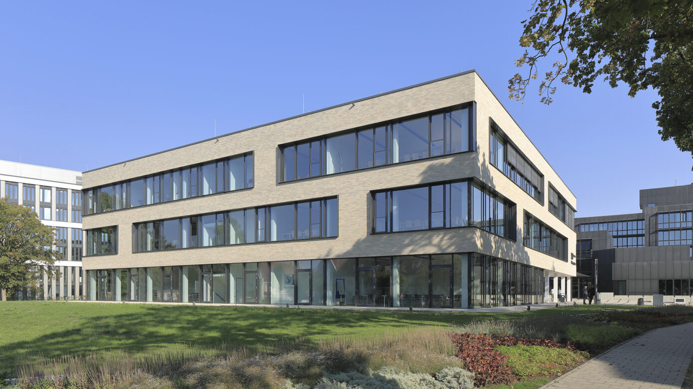 IHK-Nord Westphalen Münster mit großen Fenstern und grüner Umgebung unter blauem Himmel.