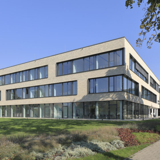 IHK-Nord Westphalen Münster mit großen Fenstern und grüner Umgebung unter blauem Himmel.