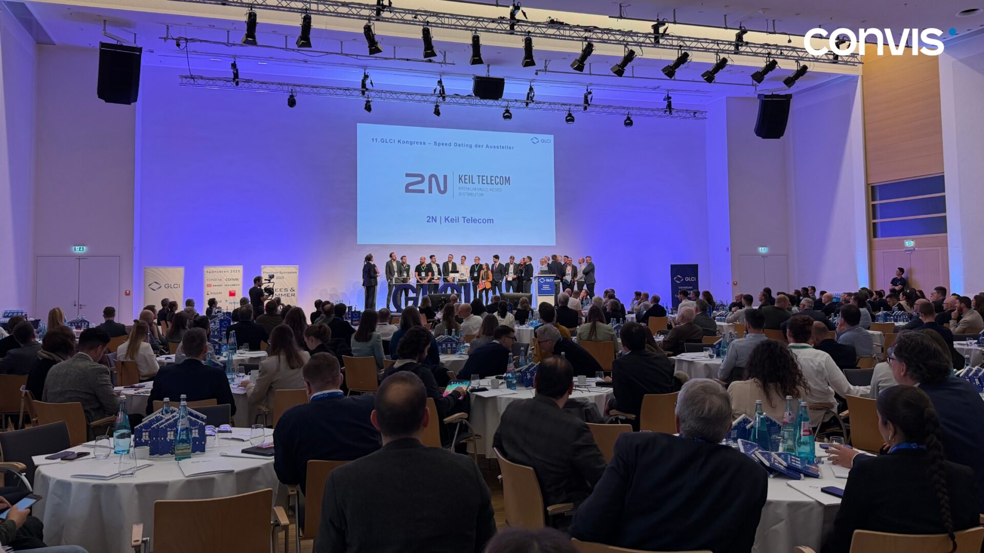 Konferenz mit Präsentation von 2N und Publikumsinteraktion im Hintergrund.