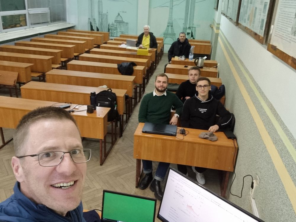 Gruppenfoto in einem leeren Klassenzimmer mit Studierenden und Dozenten.