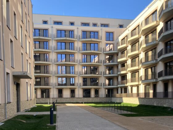 Moderne Wohnanlage mit begrüntem Innenhof und gepflastertem Weg zwischen den Gebäuden.