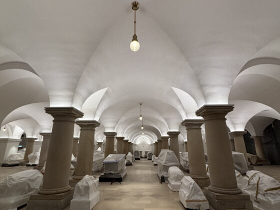 Historischer Gewölbekeller mit Säulen und verpackten Objekten, sanft beleuchtet.