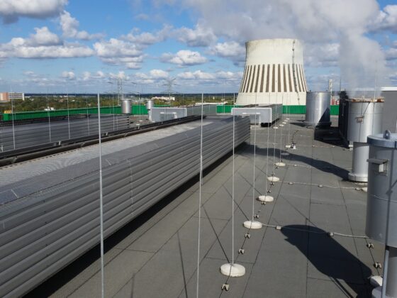 Dachansicht mit Kühlturm und Rohren, unter blauem Himmel mit Wolken.