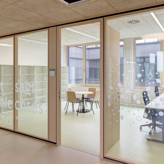 Moderne Schulräume mit Glaswänden und kreativen Sprüchen für inspirierende Arbeitsatmosphäre.