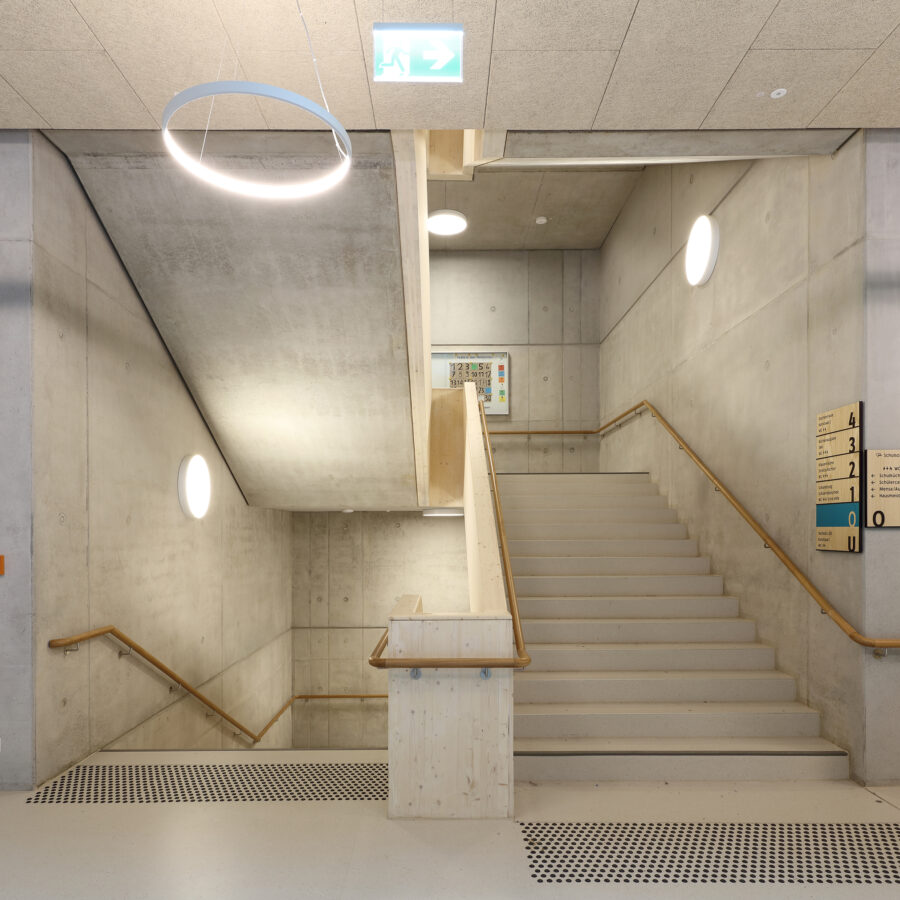 Moderne Treppe in einem minimalistischen Gebäude mit Betonwänden und Holzdetails.