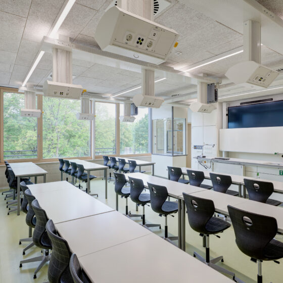 Moderne Klassenräume mit Tischen, Stühlen und digitaler Präsentationstechnik.