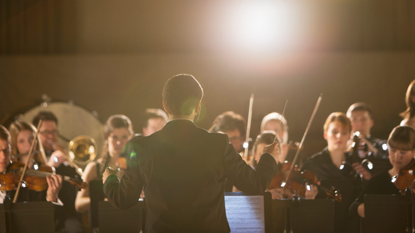 Orchesteraufführung mit Dirigent und Musikern in eleganter Abendgarderobe.