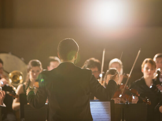 Orchesteraufführung mit Dirigent und Musikern in eleganter Abendgarderobe.