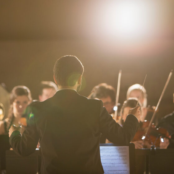 Orchesteraufführung mit Dirigent und Musikern in eleganter Abendgarderobe.