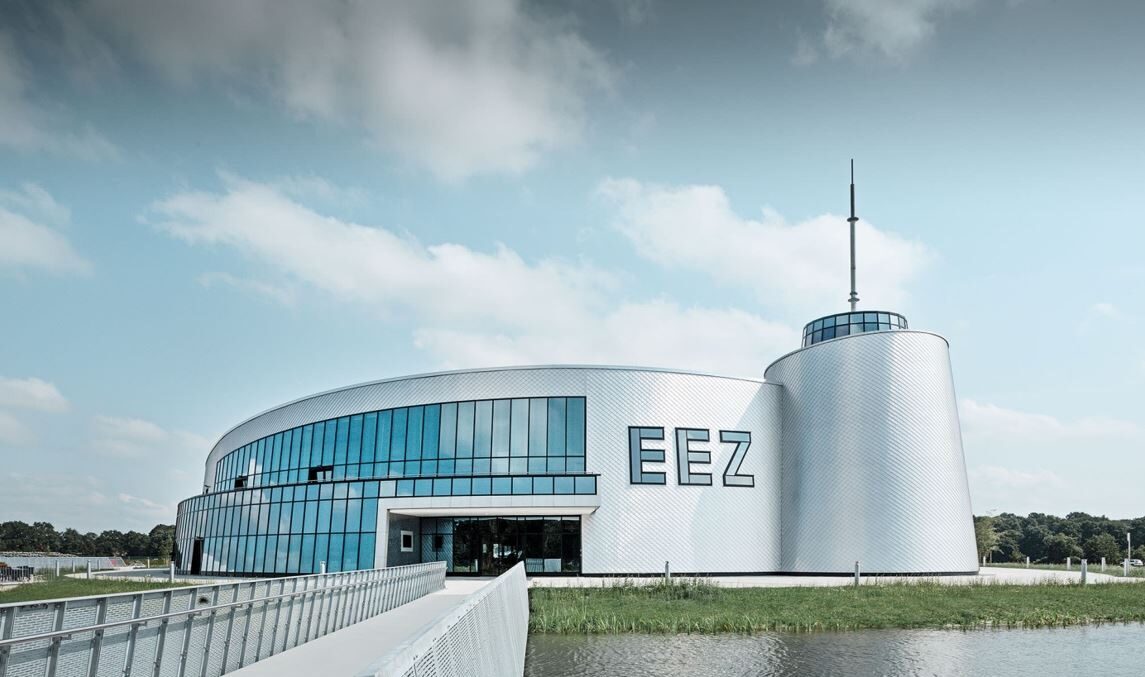 Modernes Gebäude des EEZ mit Glasfassade und umliegendem Wasser, ideal für Besucher.