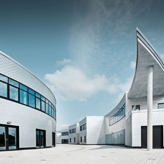 Moderne Architektur mit geschwungenen Formen und großen Fenstern unter blauem Himmel.