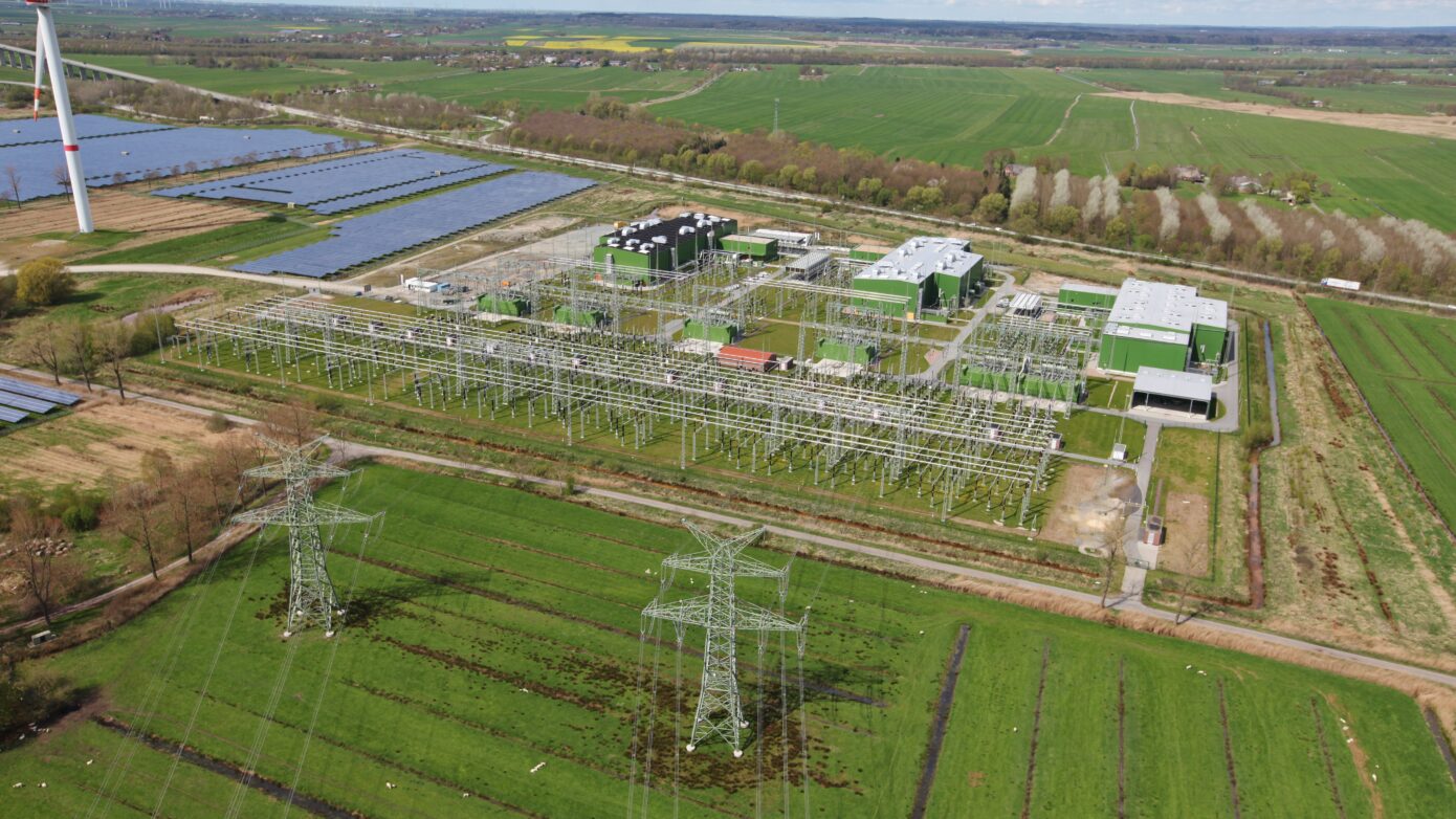 Ansicht BorWin6 mit Windkraft, Solarpanelen und Hochspannungsleitungen in ländlicher Umgebung.