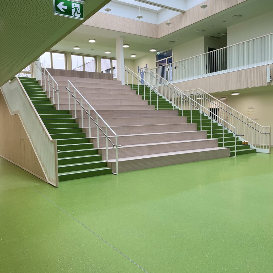 Moderne Treppe mit grünen Stufen in einem hellen, einladenden Innenraum in der Astrid-Lindgren-Grundschule