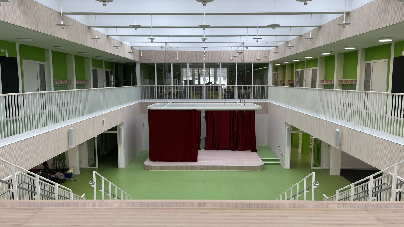 Astrid-Lindgren Schule von innen mit grünen Wänden, Bühne und großzügigem, lichtdurchflutetem Raum.