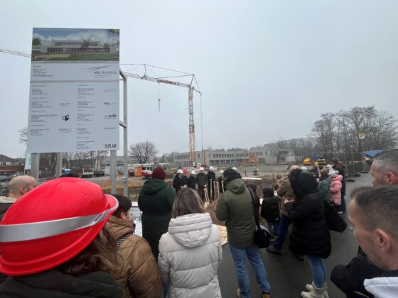 Grundsteinlegung eines neuen Bauprojekts mit zahlreichen Teilnehmern und Baukran im Hintergrund.