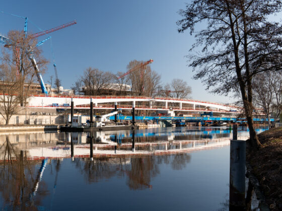 Bauarbeiten am Wasser mit Kränen und reflektierender Oberfläche im Vordergrund.