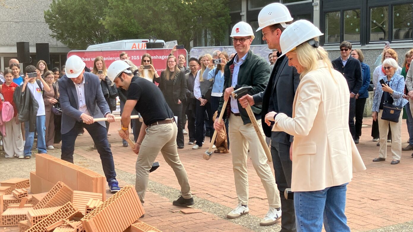Baustellenfeier: Personen in Helmen schlagen mit Werkzeugen auf Ziegelsteine.