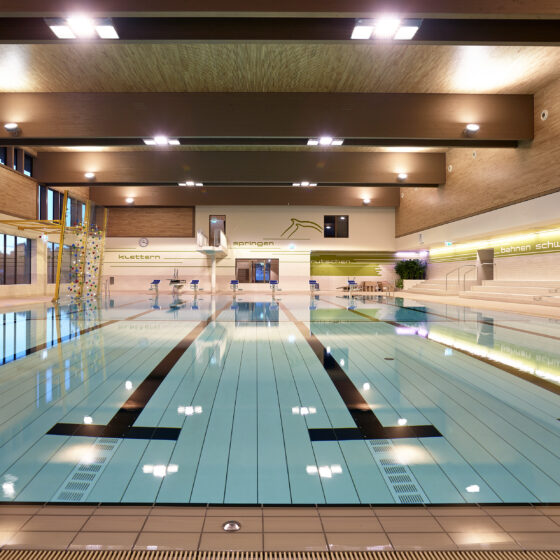 Modernes Hallenbad mit Schwimmbecken, Sprungturm und Holzverkleidung für Sport und Freizeit.