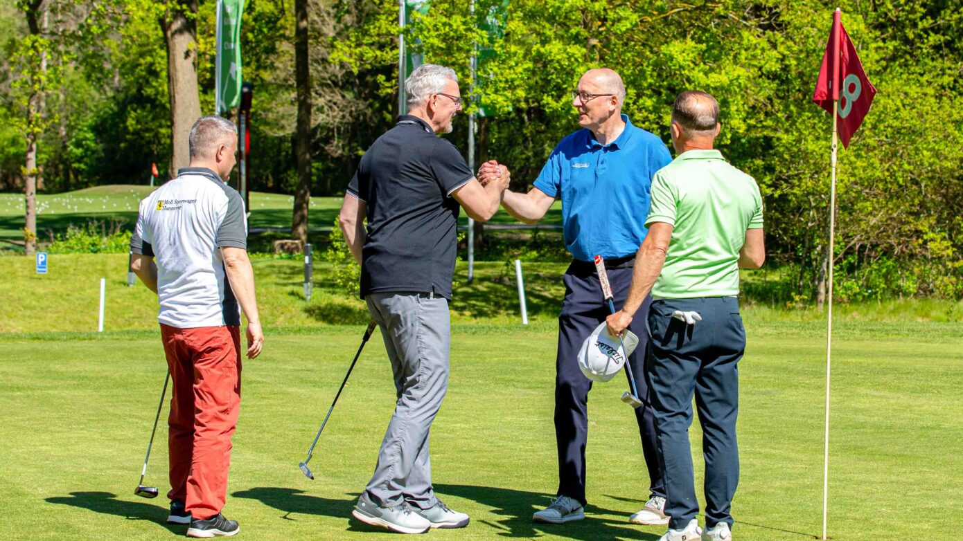 Freundliches Golfspiel: Vier Männer feiern einen gelungenen Schlag auf dem Golfplatz.
