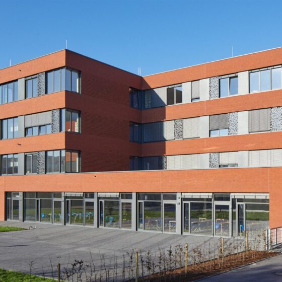 Integrierte Gesamtschule Ibbenbüren mit roten Ziegeln und großen Fenstern in sonniger Umgebung.