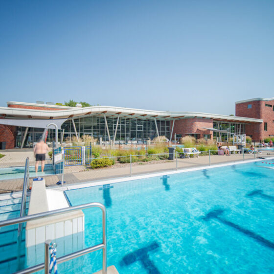Kombibad „Aqua Reini“ in Rheine von Außen mit Hallenbad, Außenpool und Rutschen an einem sonnigen Tag.