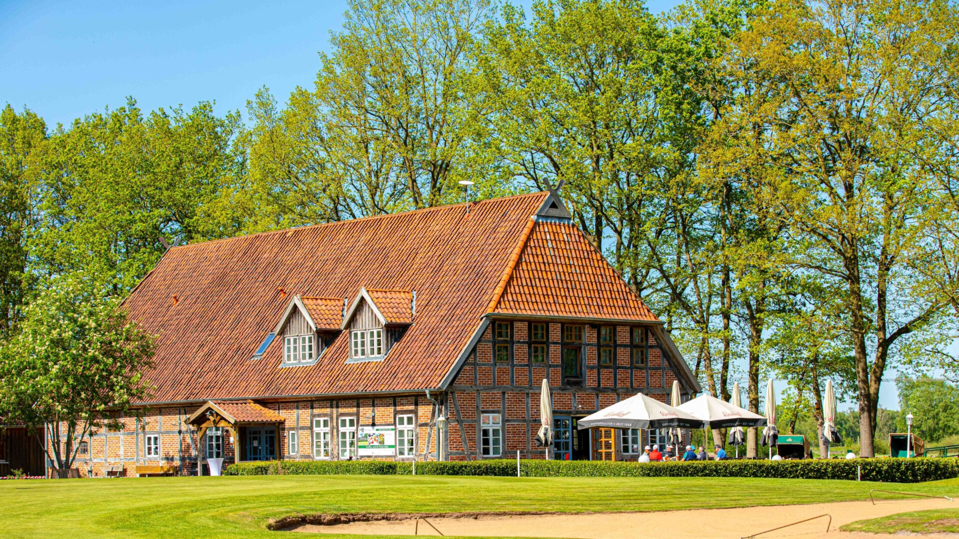 Historisches Fachwerkhaus umgeben von Bäumen und grünem Garten, ideal für Veranstaltungen.