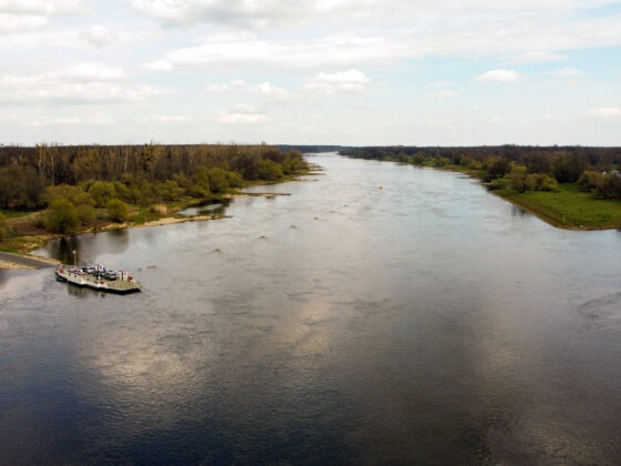 Flusslandschaft mit Boot und grünen Ufern unter einem bewölkten Himmel.