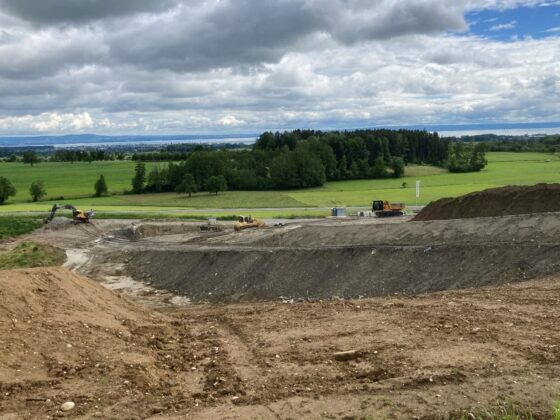 Baustelle mit Baggern in einer grünen Landschaft unter bewölktem Himmel.