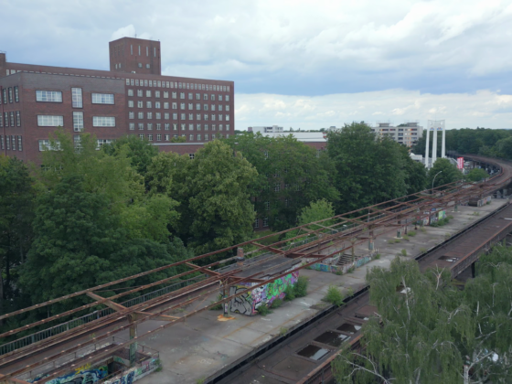 Verlassene Hochbahntrasse mit Graffiti, umgeben von Bäumen und urbaner Architektur.