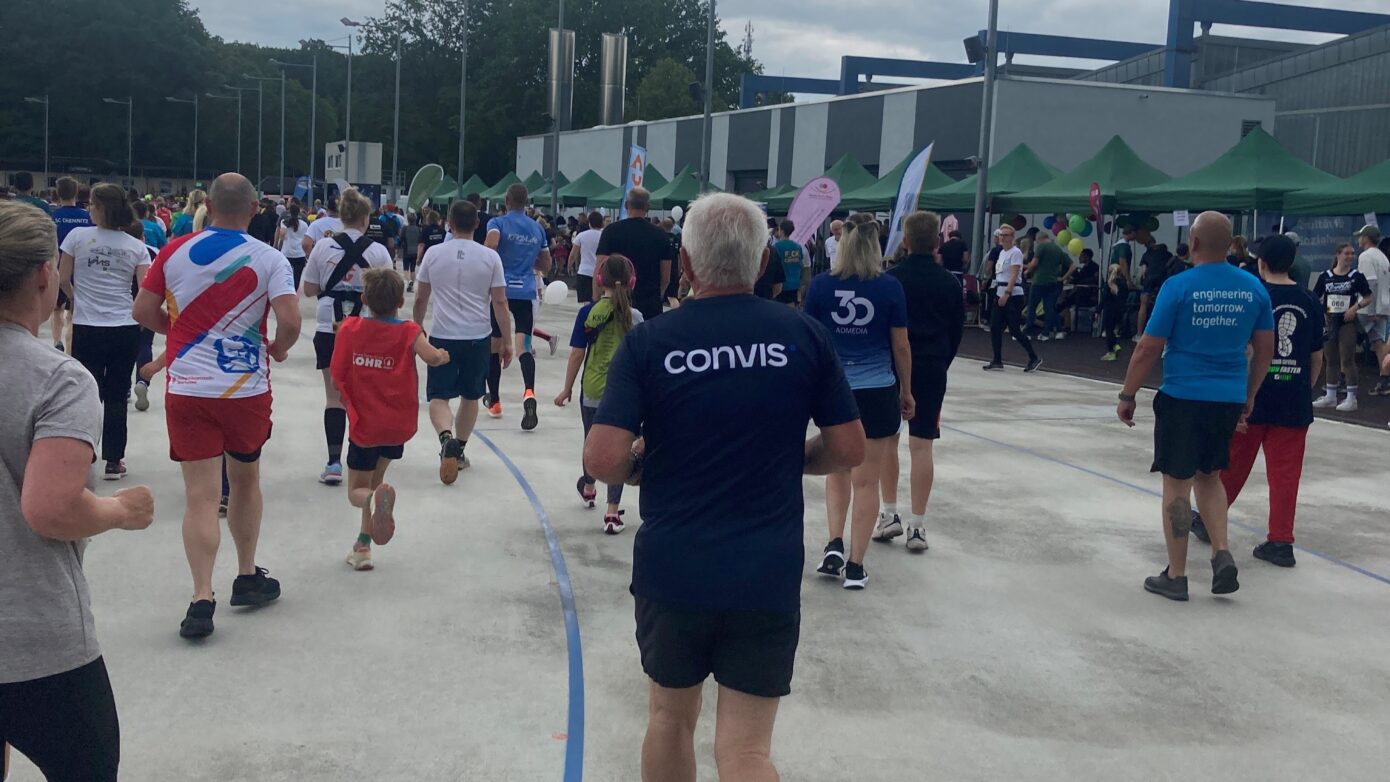 Teilnehmer eines Lauf-Events bewegen sich auf einer Strecke unter bewölktem Himmel.