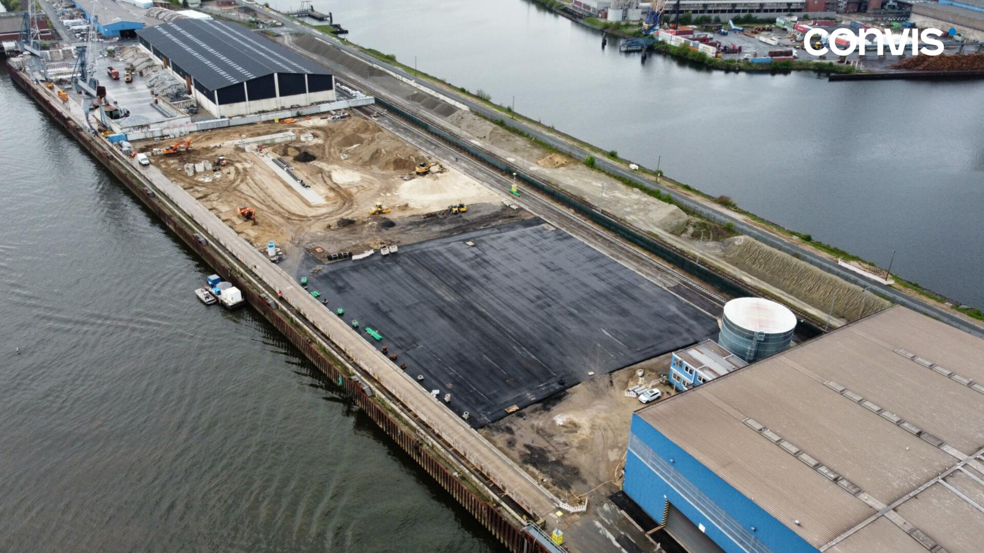 Bauarbeiten im Hafen mit Maschinen und neuem Asphaltbelag am Wasser.