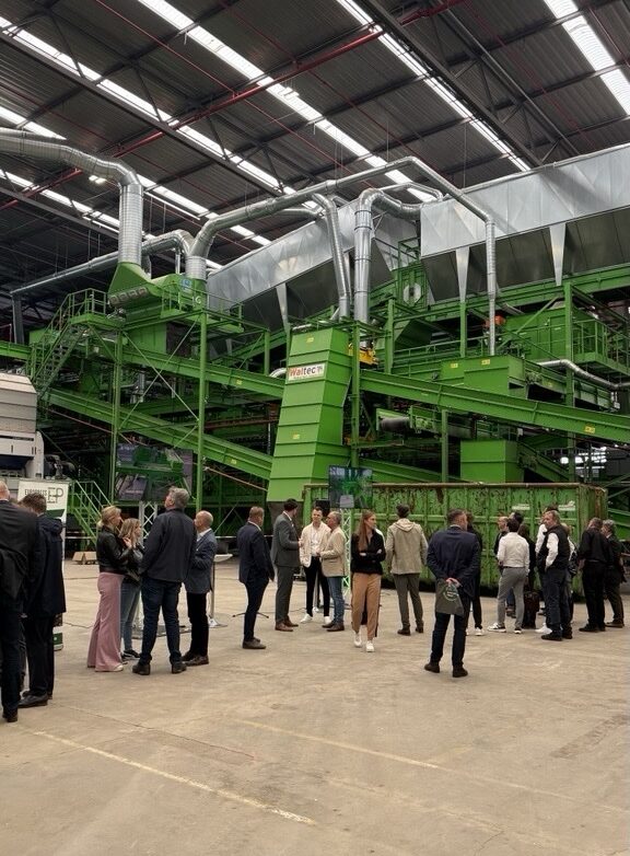 Besuchergruppe in einer modernen Recyclinganlage mit grüner Maschinenausstattung.