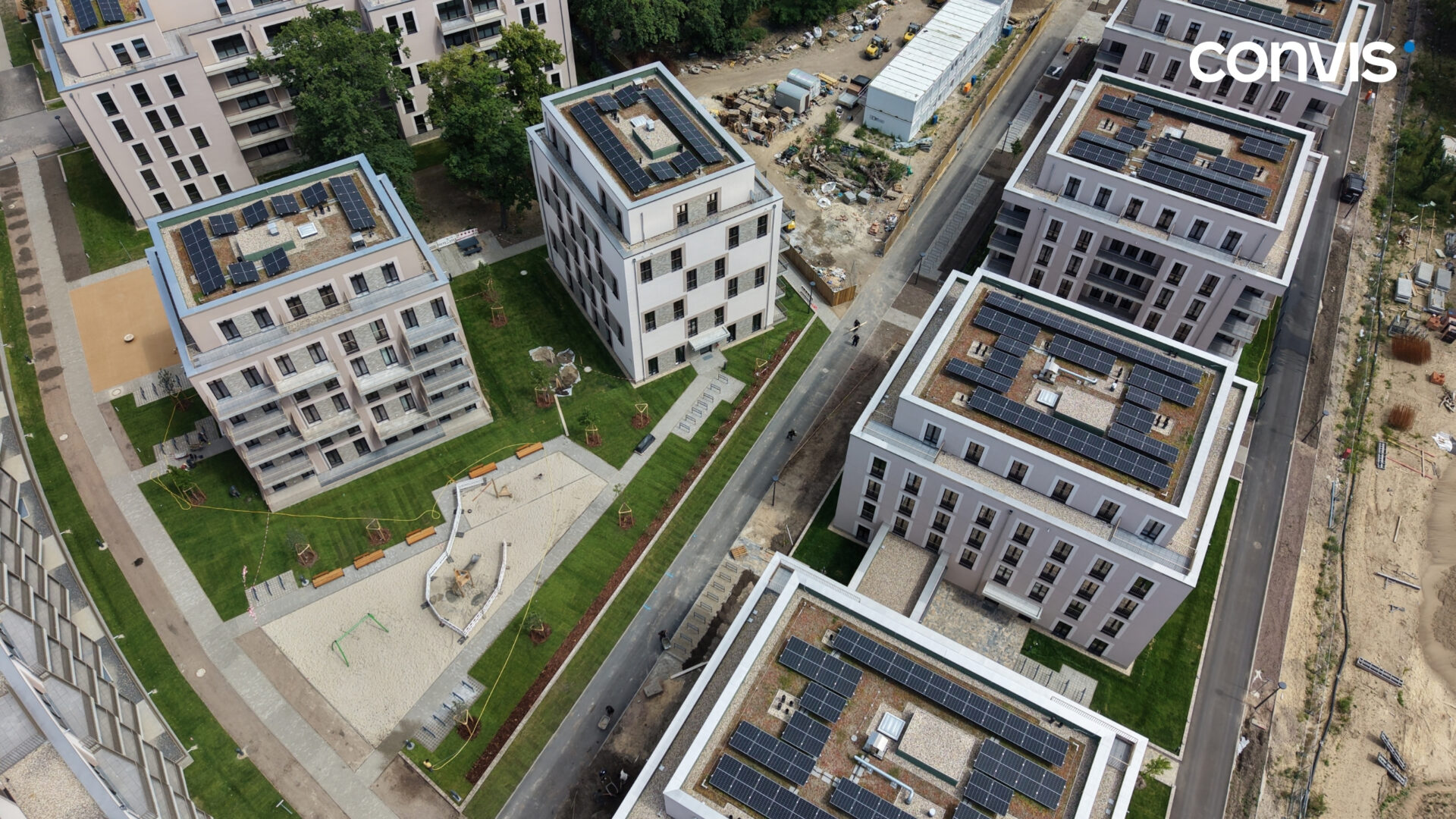Moderne Wohnanlage mit Solaranlagen, Spielplatz und grünen Flächen aus der Vogelperspektive.