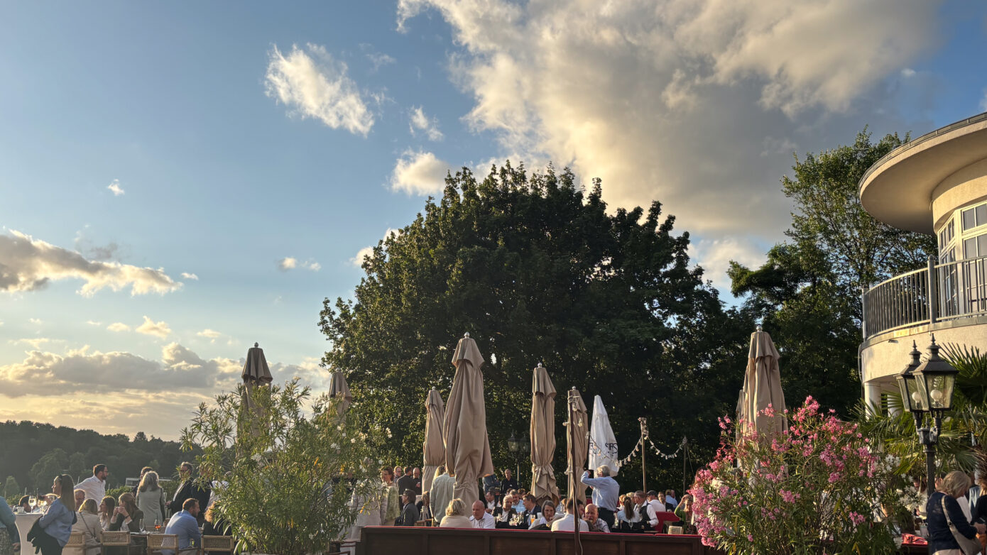 Gemütliches Restaurant im Freien mit Gästen, Bäumen und schönem Himmel bei Sonnenuntergang.