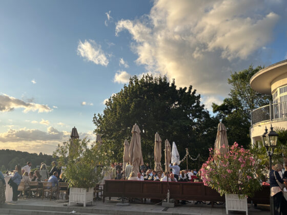 Gemütliches Restaurant im Freien mit Gästen, Bäumen und schönem Himmel bei Sonnenuntergang.