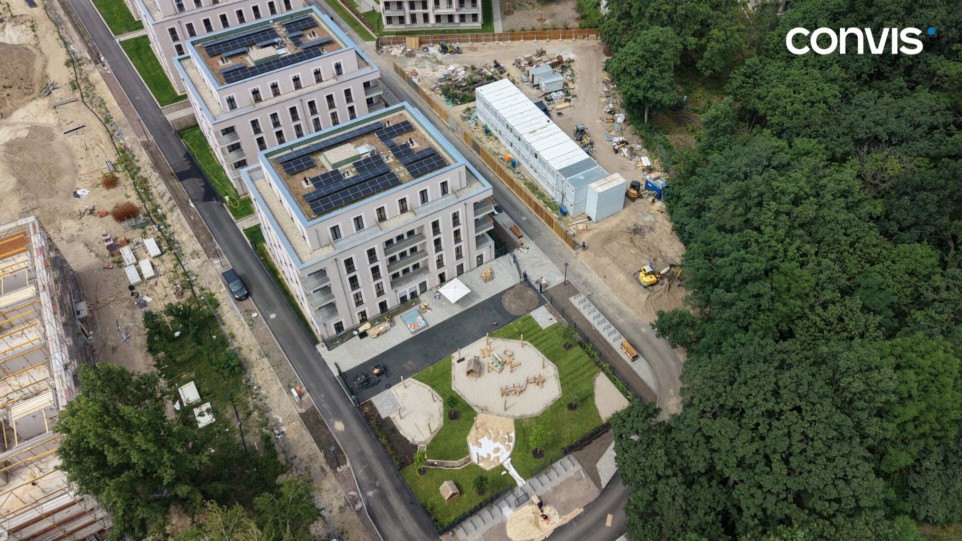 Moderne Wohnanlage mit Spielplatz und Baustelle in grüner Umgebung.