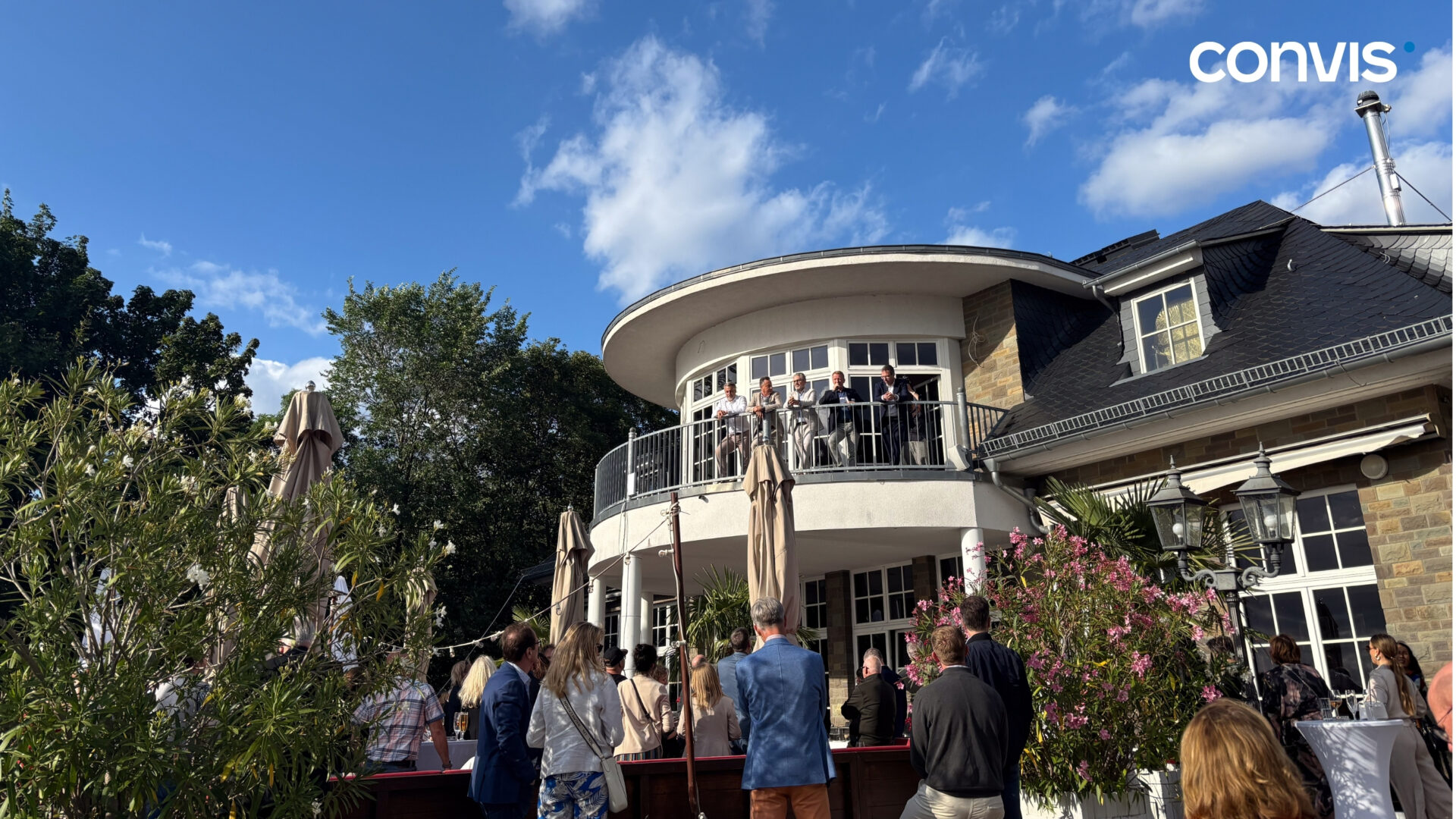 Festliche Veranstaltung auf der Terrasse eines stilvollen Gebäudes mit Gästen und schöner Kulisse.