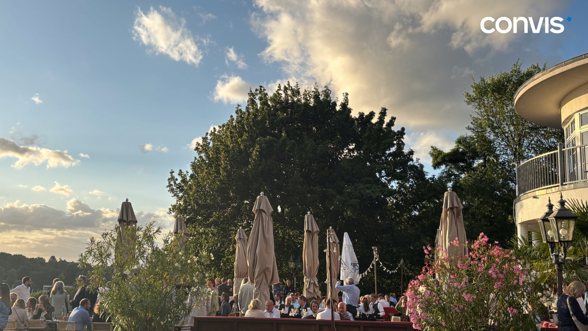 Gemütliche Außenterrasse mit Gästen, Bäumen und Wolken im Abendlicht.