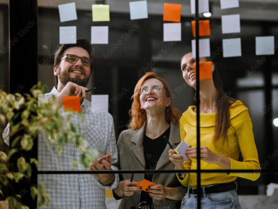 Team brainstormt mit Haftnotizen an einem Fenster in modernem Büro.