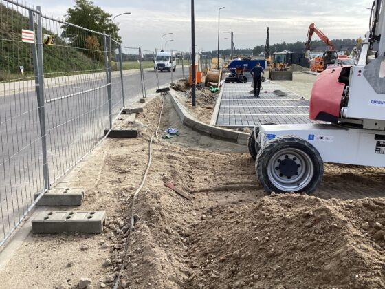 Baustelle mit Maschinen, Schutt und Bauzäunen an einer Straße.