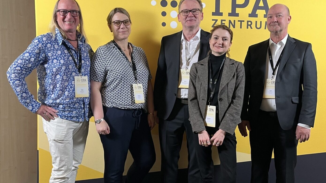 Gruppenfoto von Fachleuten vor einem IPA-Zentrum Banner auf einer Konferenz.