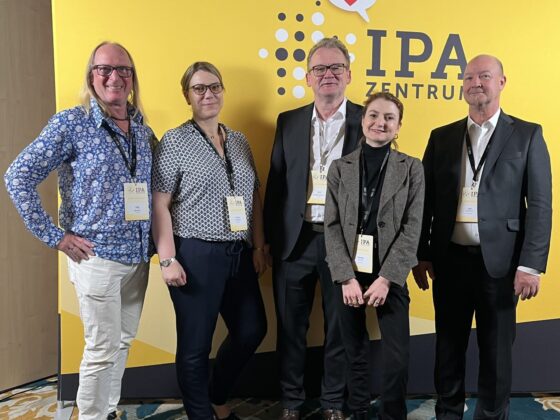 Gruppenfoto von Fachleuten vor einem IPA-Zentrum Banner auf einer Konferenz.