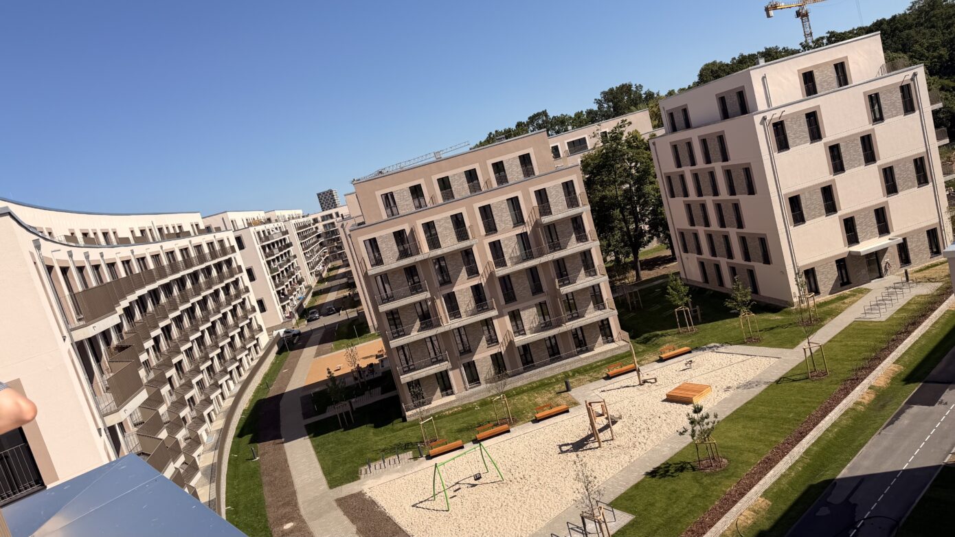 Moderne Wohnanlage mit Spielplatz und großzügigen Grünflächen unter blauem Himmel.