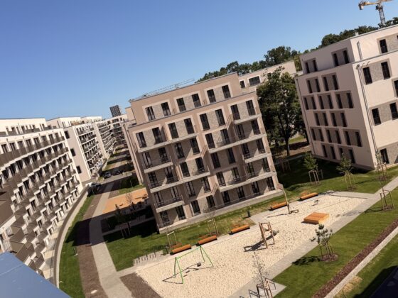 Moderne Wohnanlage mit Spielplatz und großzügigen Grünflächen unter blauem Himmel.