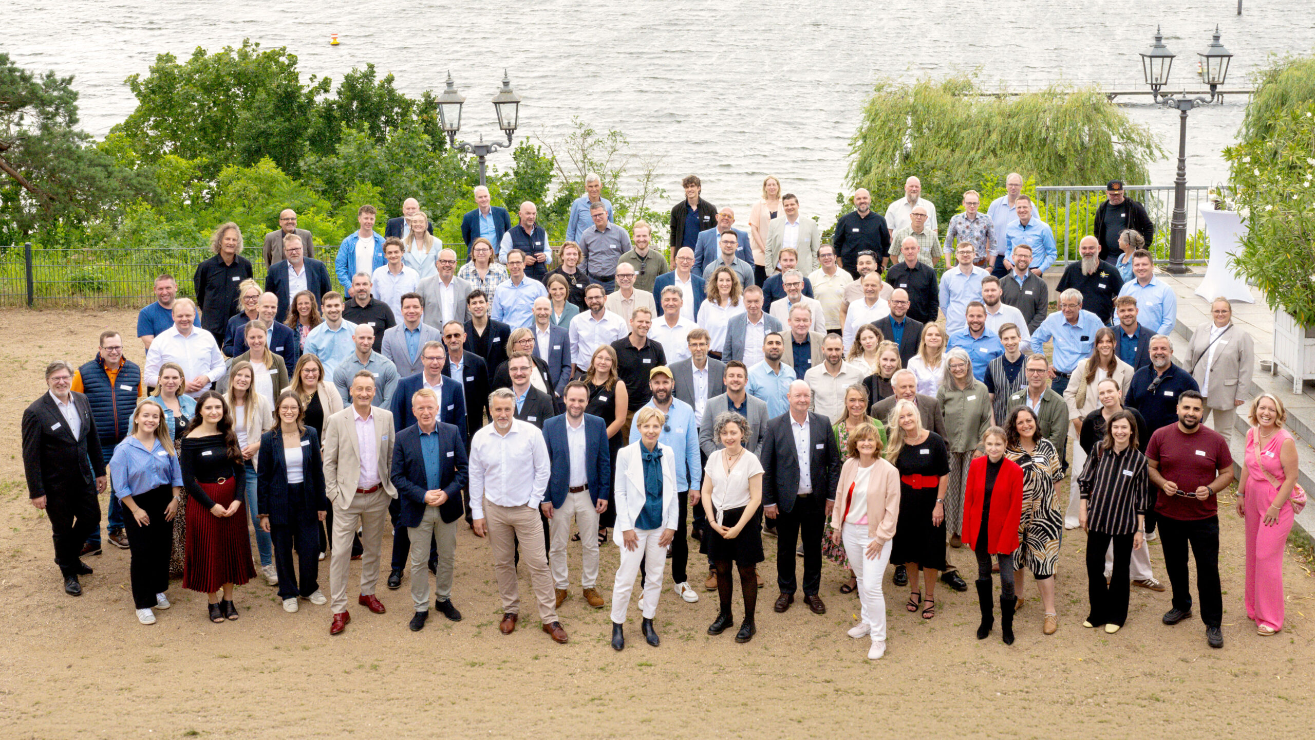Gruppenfoto von über 100 Personen (convis-Mitarbeitende) am Wasser, bei einer Veranstaltung im Freien.