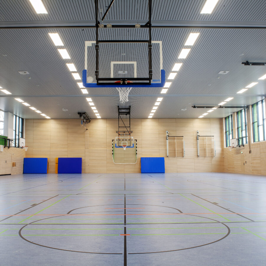 Helle Sporthalle mit Basketballkorb und modernen Trainingsflächen für verschiedene Sportarten.