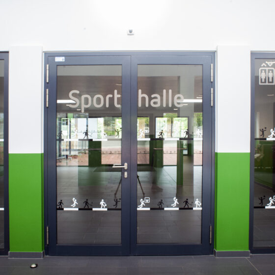Moderne Sporthalle mit Glasfront und sportlichen Symbolen an der Wand.