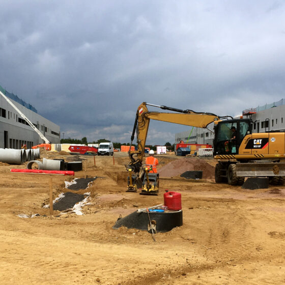 Bauarbeiter und Maschinen auf einer Baustelle mit Wolken am Himmel.